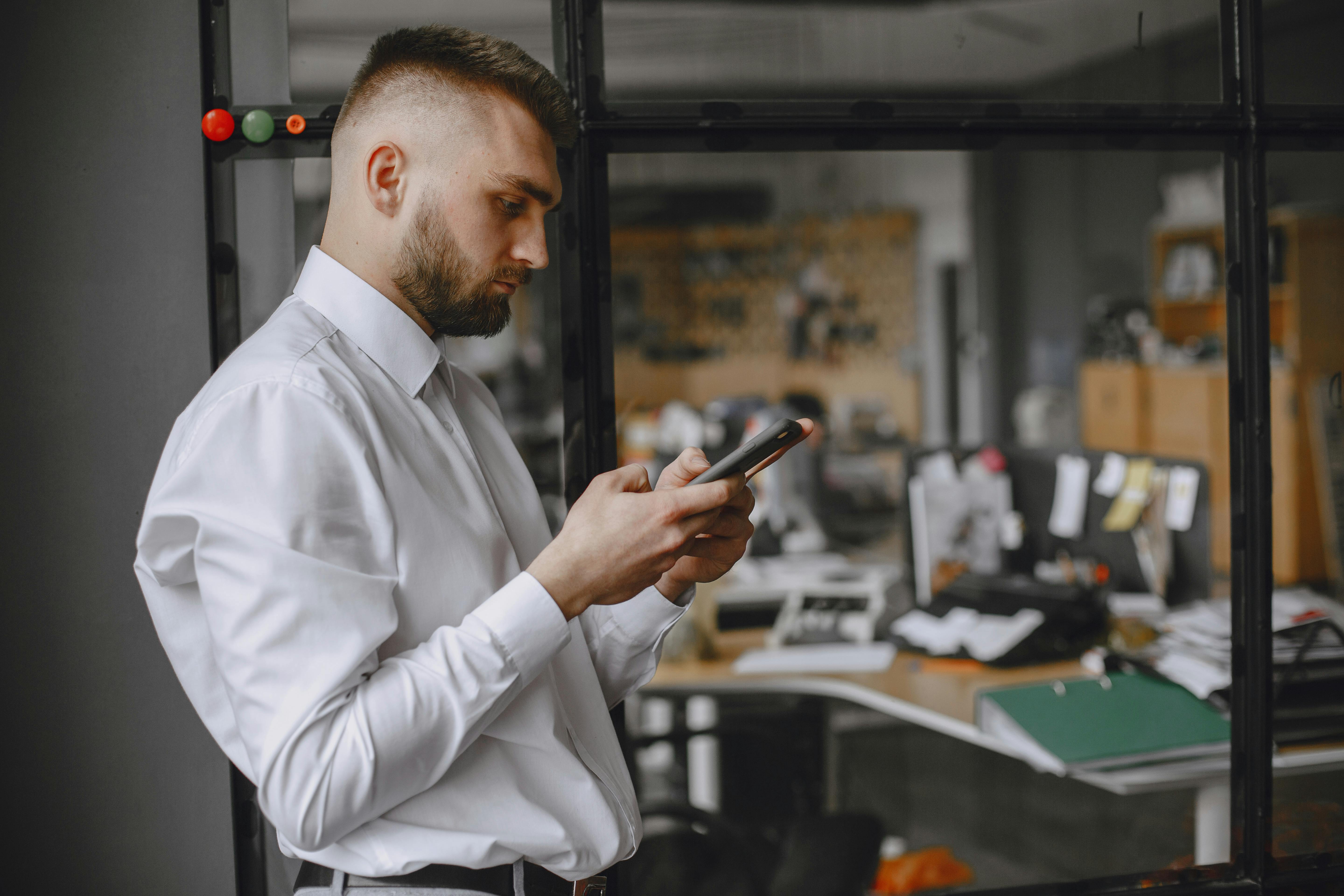Businessman in white shirt using phone in office, showcasing modern technology and workplace focus.