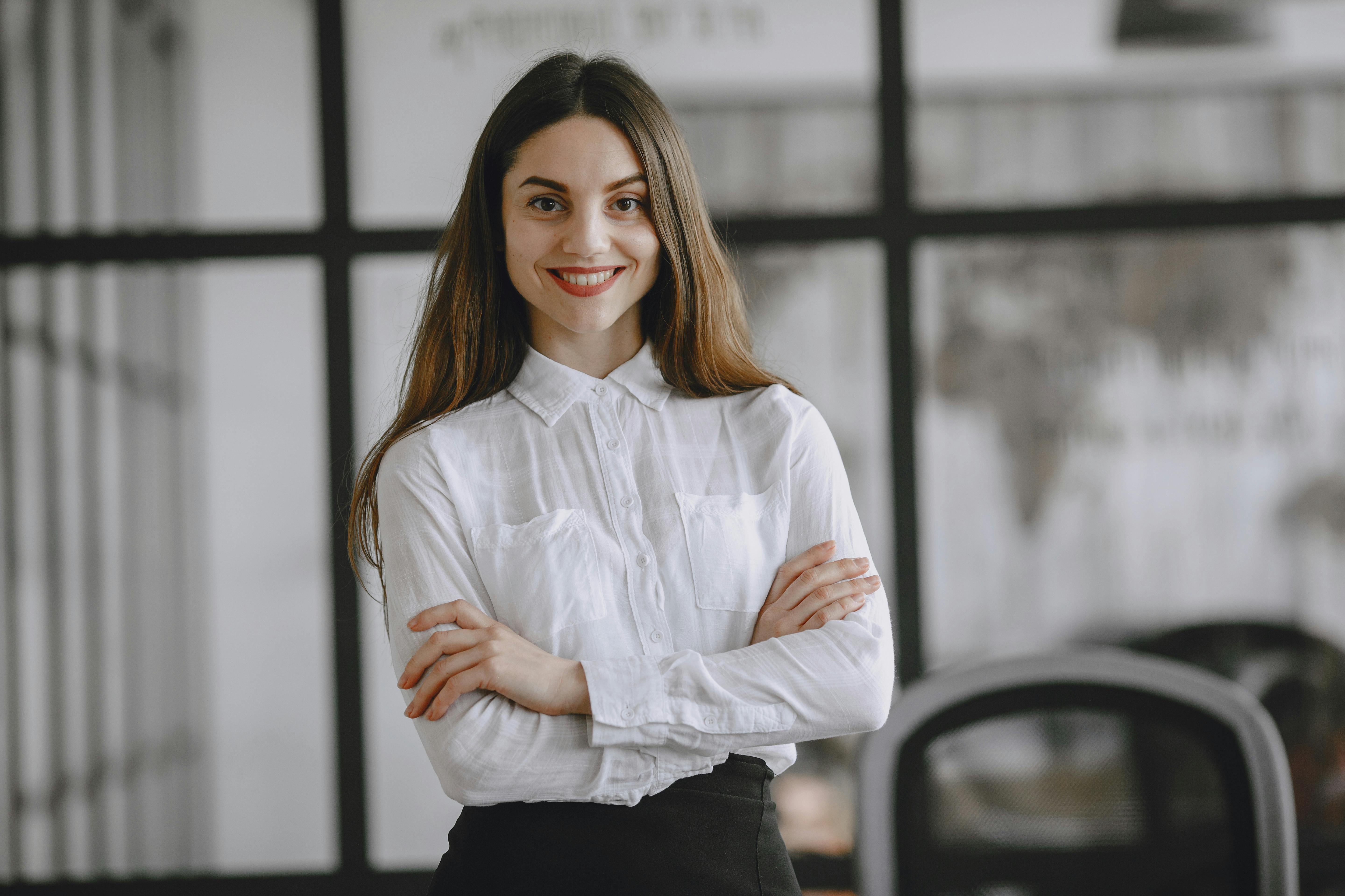 Confident woman with long brown hair standing indoors smiling in an office environment.