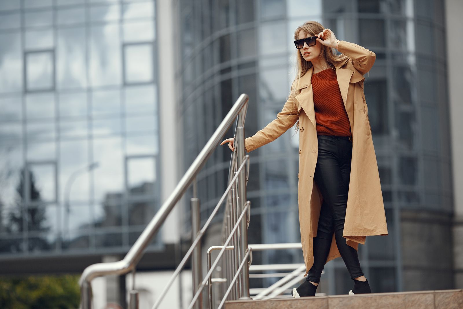 Woman in a trench coat on steps by a glass building