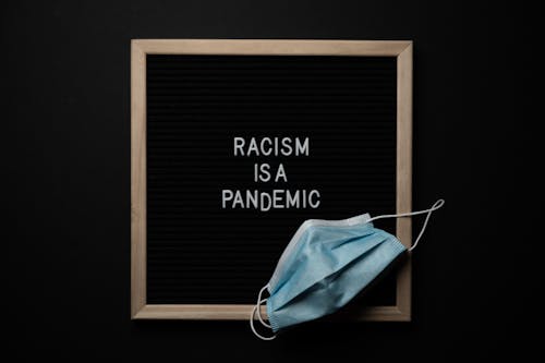 Free Disposable mask on blackboard with Racism Is A Pandemic title Stock Photo
