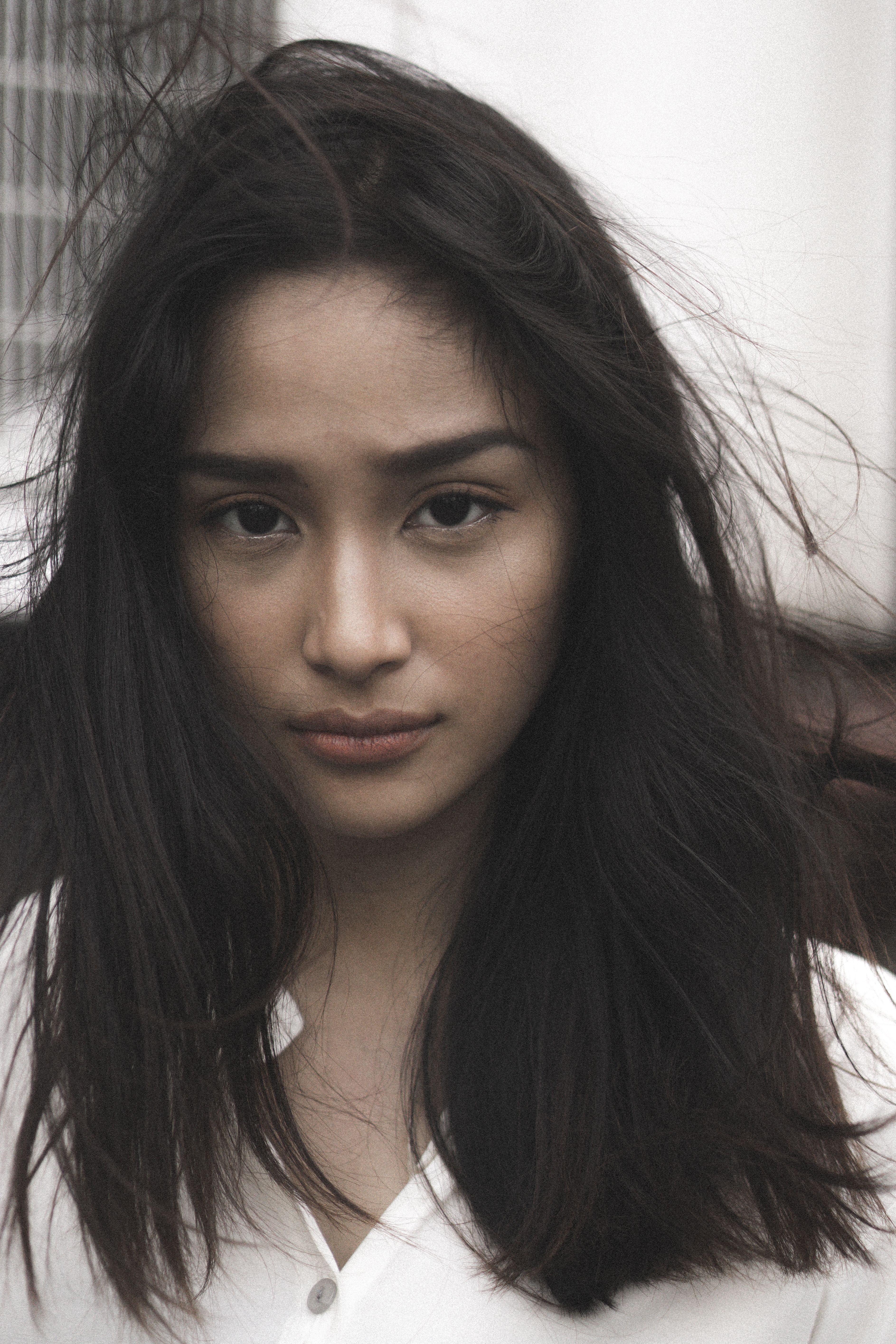 Close-up portrait of a young woman with long hair and serene expression, standing outdoors.