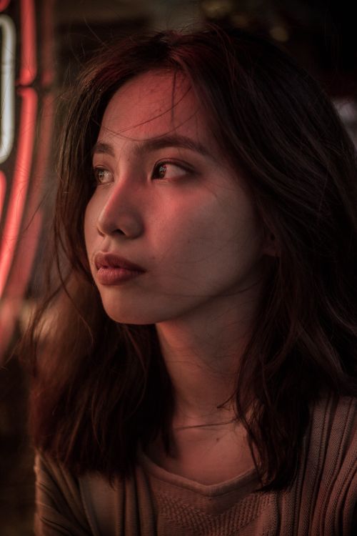 Free Portrait of a young woman looking away in a dimly lit urban environment, capturing a thoughtful moment. Stock Photo