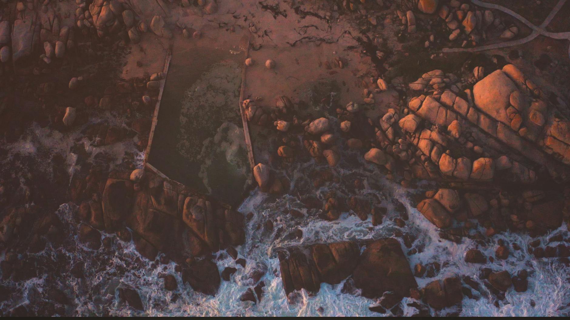 Aerial view of an ocean pool with waves crashing over the edge.