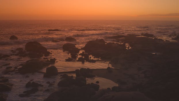 A stunning view of Cape Town's rocky coast at sunset with warm tones and ocean reflections.