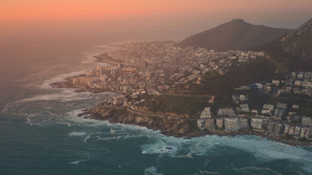 Aerial view of Cape Town's coastal cityscape with a vibrant sunset sky over the Atlantic Ocean.
