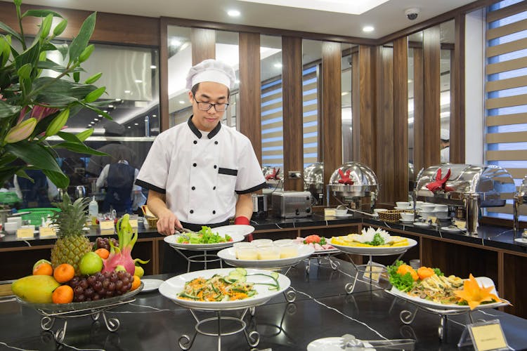 A Man Refilling Food At A Buffet