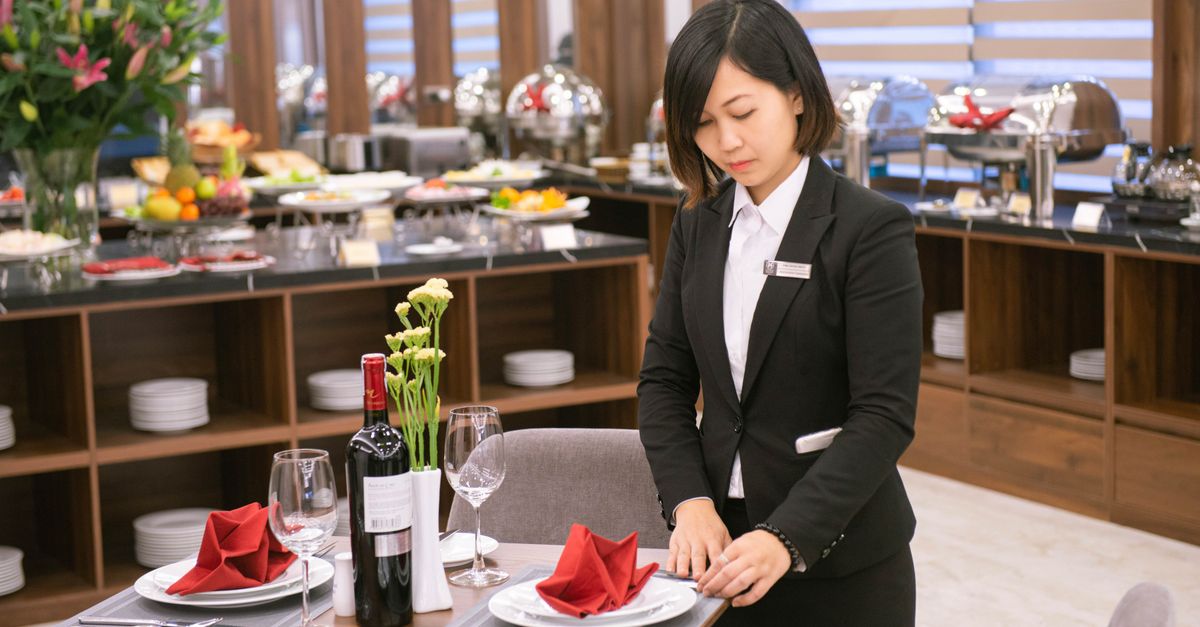 Asian waitress setting an elegant table in a Hanoi restaurant, creating a formal dining experience.