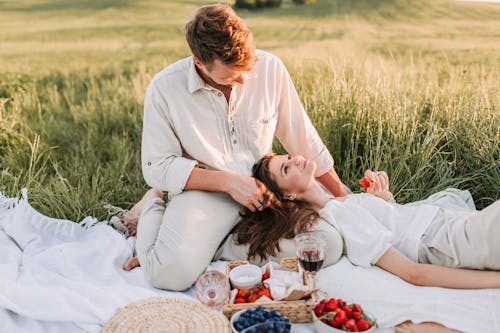 Couple enjoying a romantic picnic outdoors in lush green field, eating strawberries and blueberries.
