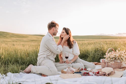 Couple Sitting on a Picnic Blanket Near Grass Field while Looking at Each Other