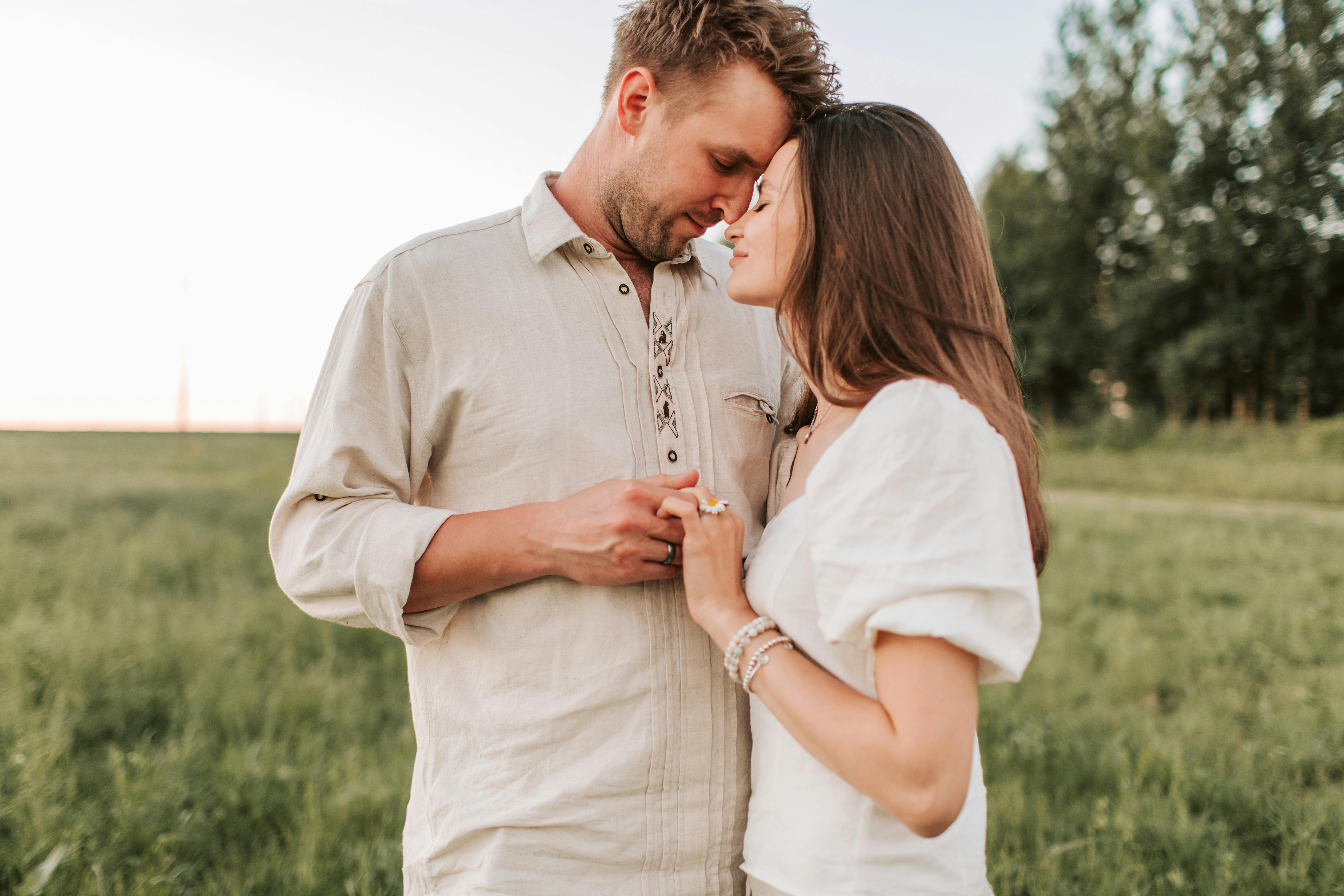 A romantic moment between a couple embracing face to face in a grassy field at sunset.