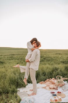 日落时分，情侣们在绿意盎然的草地上享受浪漫野餐，彼此相拥，温暖而充满爱意