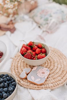 Fresh strawberries in a ceramic bowl on a woven mat, perfect for a summer picnic.