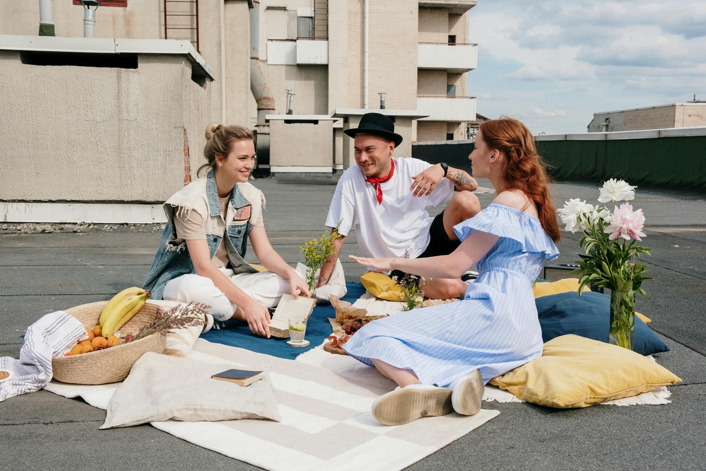 friends having a picnic on a rooftop wearing airy clothes, blue dress, and hat to shield from sun