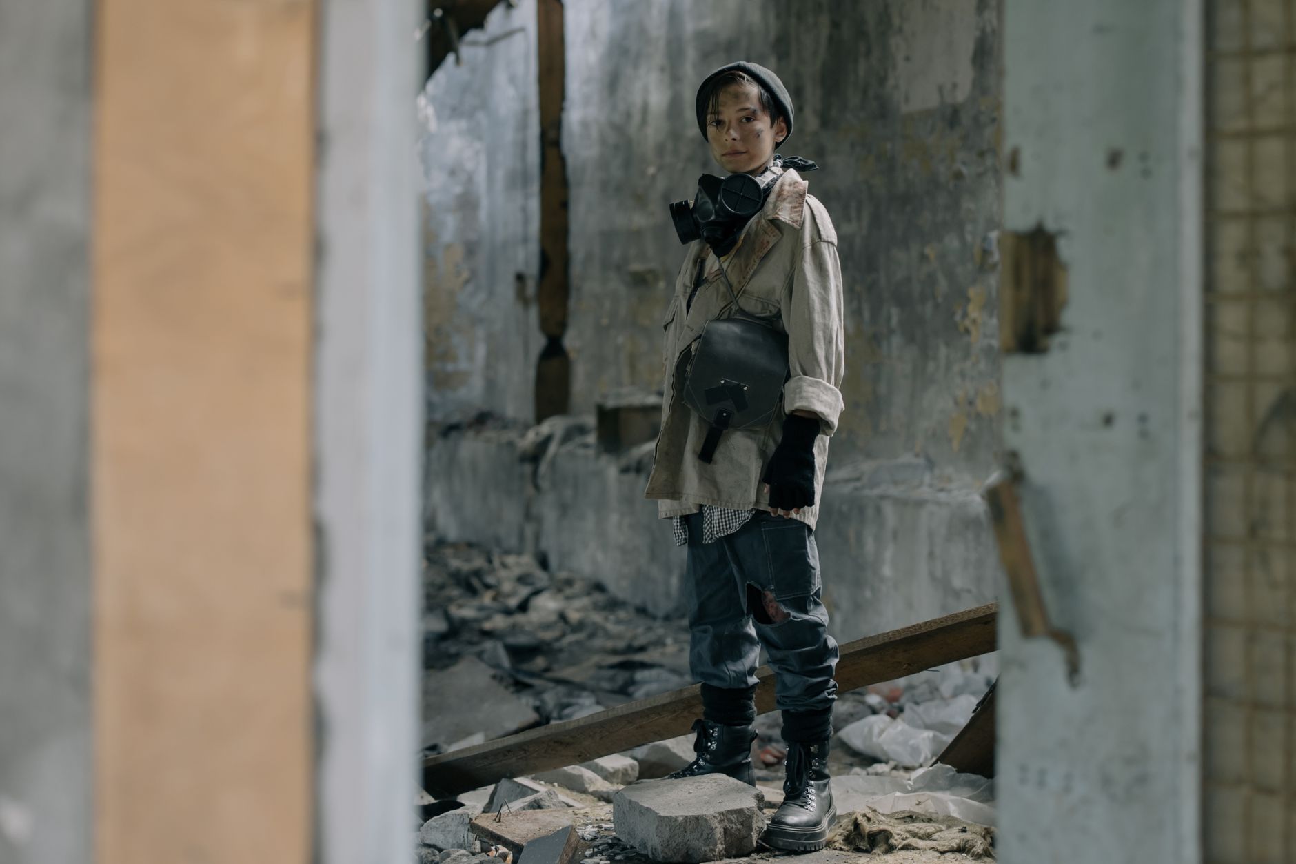 Young person in protective gear stands in a desolate, abandoned building, symbolizing survival.