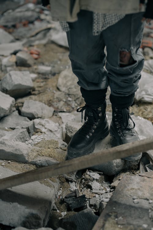 Persona In Pantaloni Neri E Stivali Di Pelle Nera In Piedi Sulla Roccia Grigia