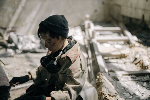 Free A young person in a desolate urban setting, wearing survival gear, evokes a post-apocalyptic atmosphere. Stock Photo