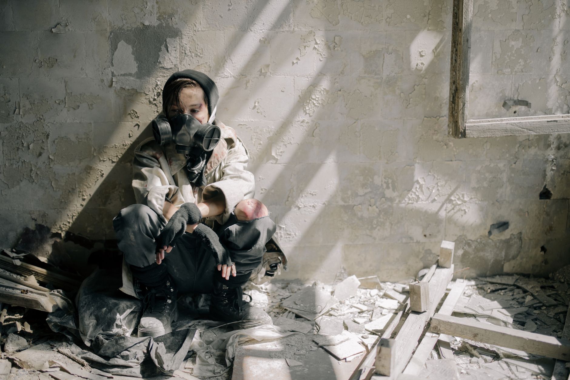 A young person in a gas mask sits in a crumbling room, symbolizing survival in an abandoned, urban environment.