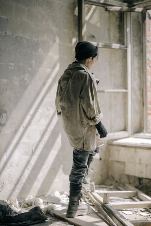 Free A lone person standing in an abandoned, decaying building looking out a window. Stock Photo