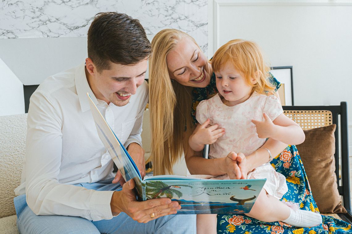 Happy family reading a book together on a sofa in a bright home