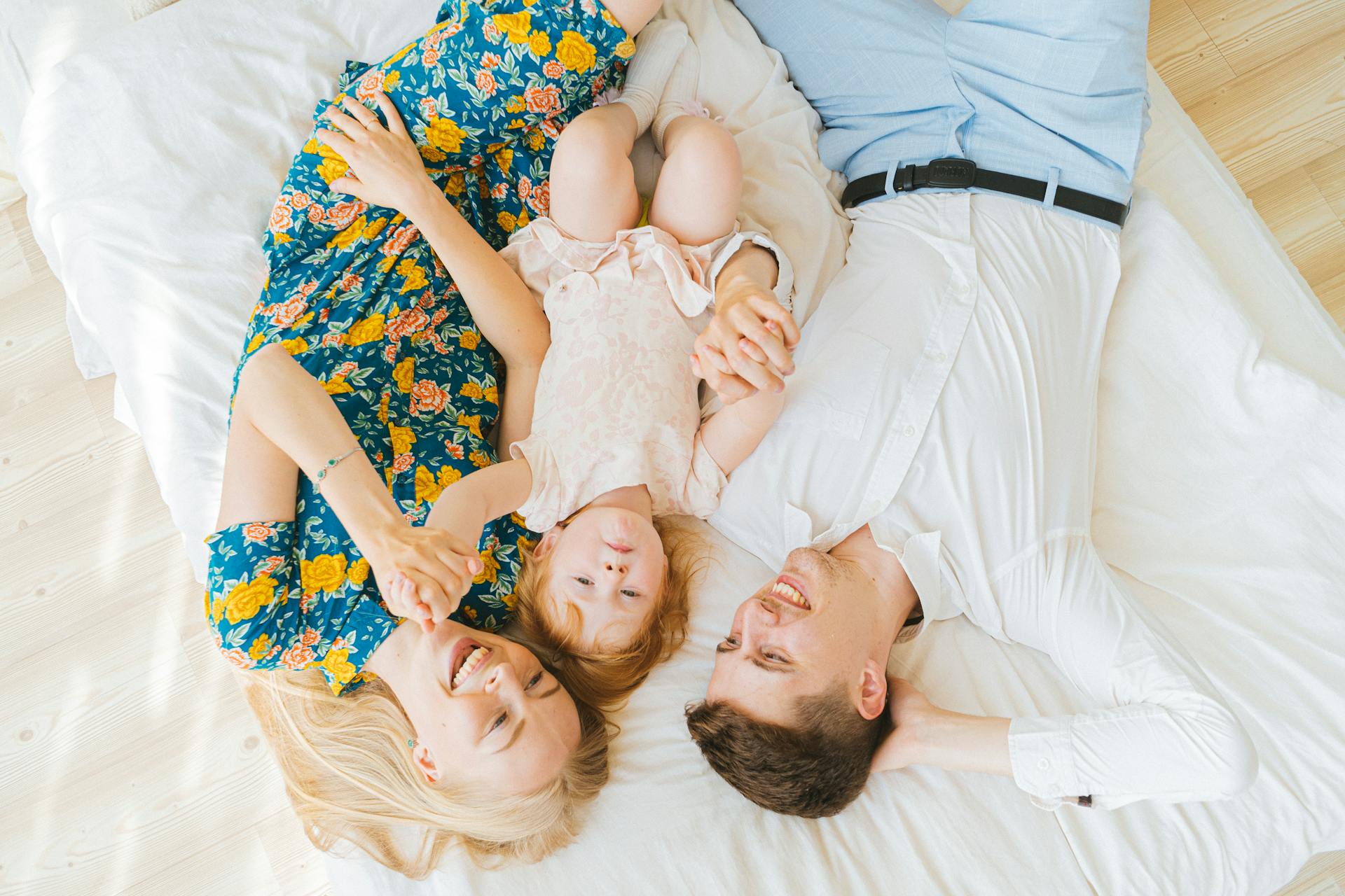 A joyful family bonding moment with parents and child lying together on a bed, smiling warmly.