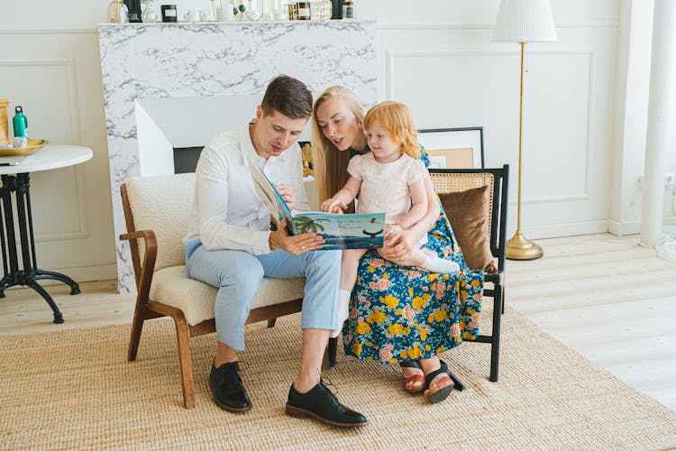 Photo Of Parents Reading A Book With Their Daughter