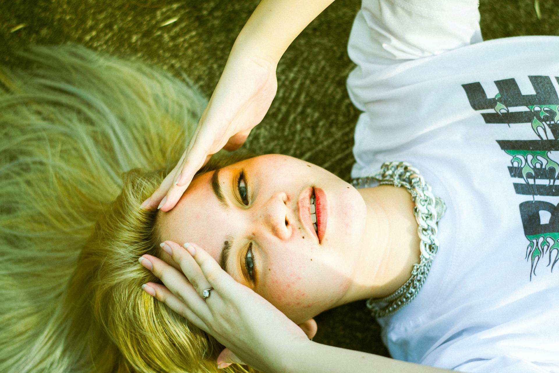 A woman with platinum blonde hair lying outdoors, hands on head, exuding a serene vibe.