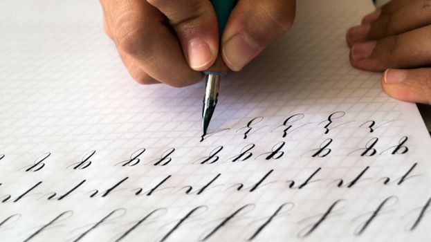 A close-up of hands practicing calligraphy with a fountain pen on paper, showing elegant handwriting.