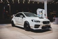 Luxury white automobile with black wheels and bright headlights on illuminated gas station at night
