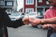 Unrecognizable male in casual clothing passing joint with marijuana to friend on street in daylight on blurred background