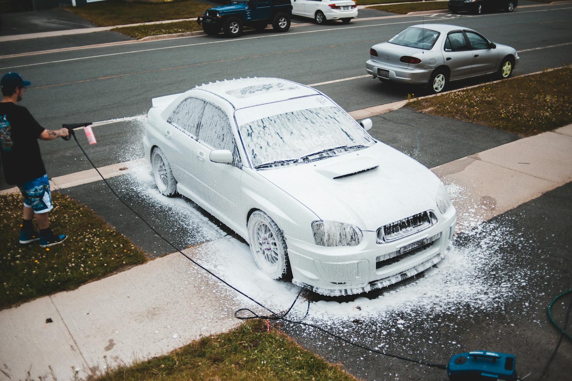 Male driver washing car with power washer