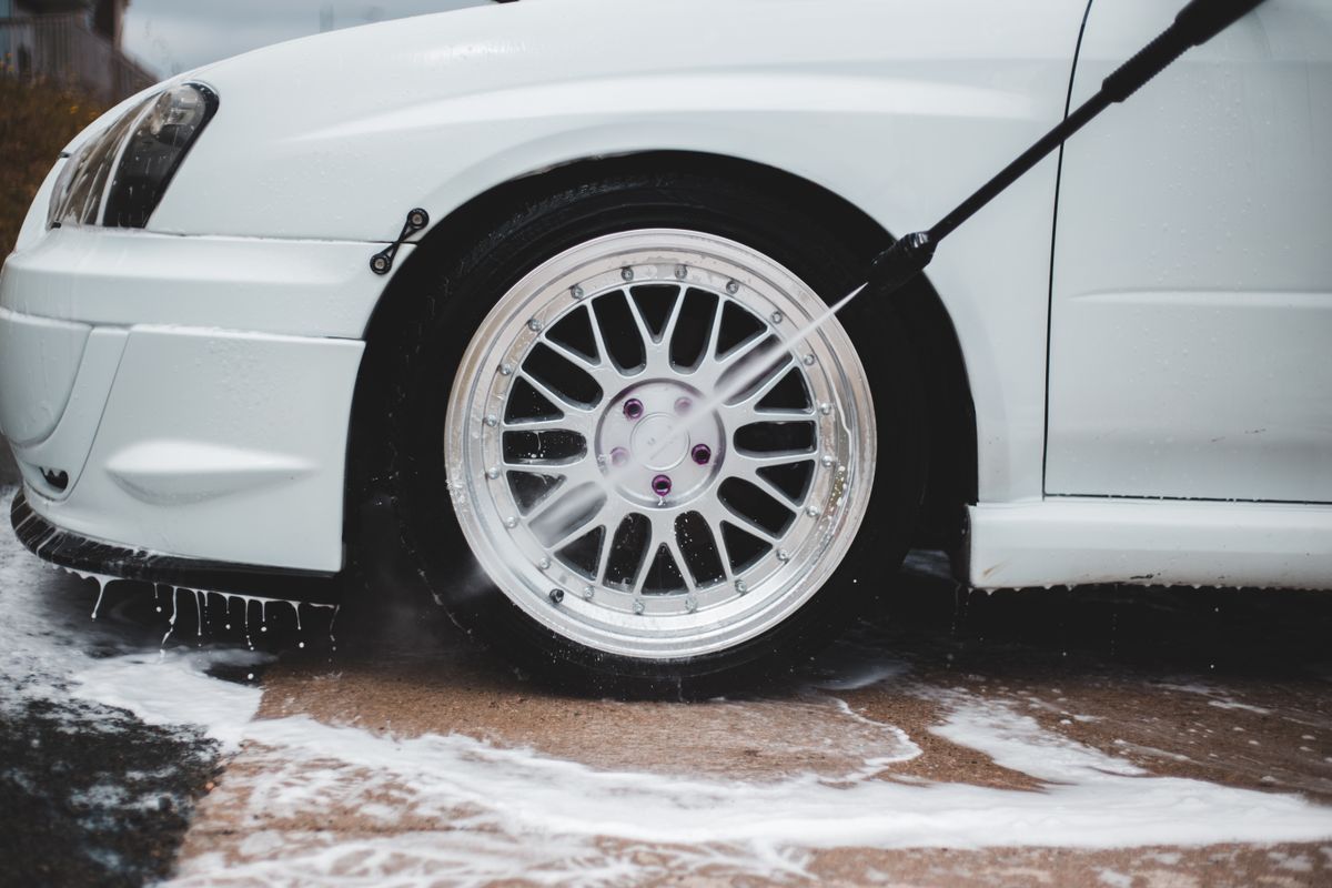 Close-up of a pressure washer nozzle spraying a rotating water and soap jet on a wheel