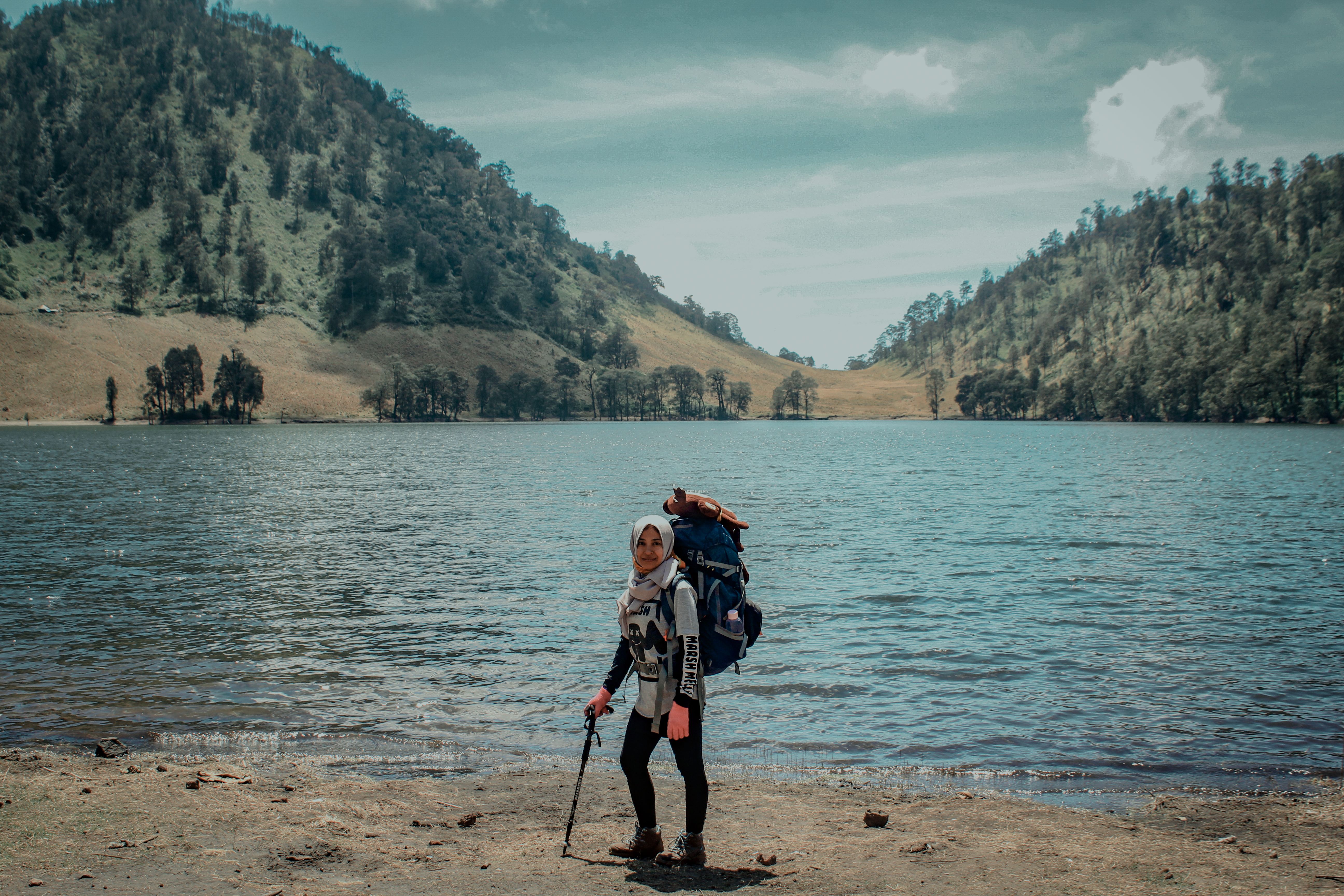 Woman wearing a hijab backpacking beside a tranquil mountain lake on a hiking adventure.