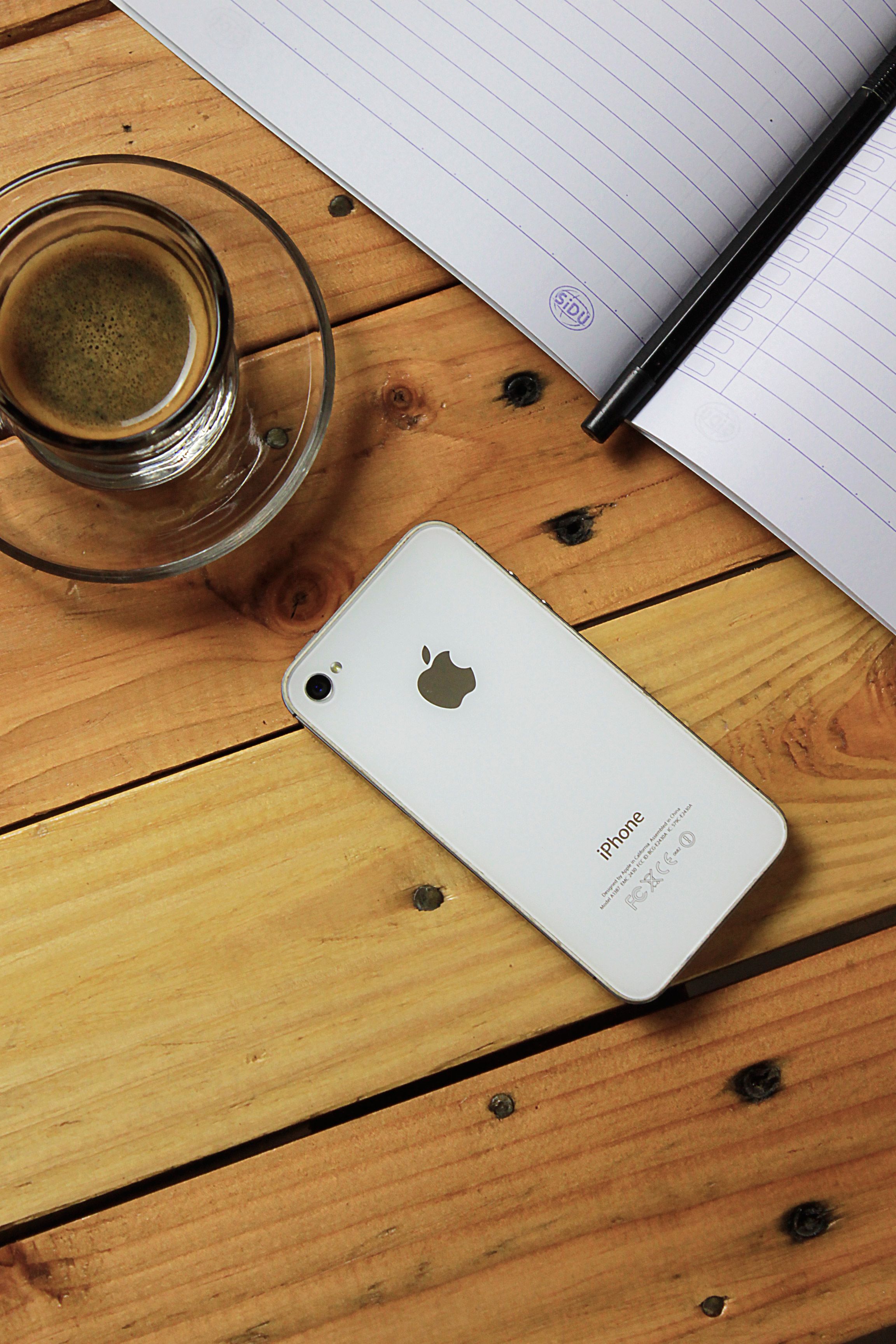A glass of coffee beside a smartphone and notebook on a wooden surface, perfect for productivity themes.