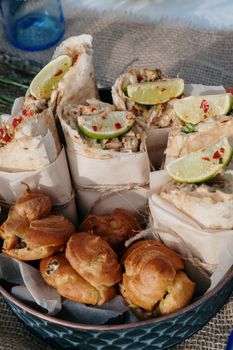 A tempting display of wraps with lime wedges and pastries set on an outdoor table.