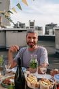 一个开朗的男人和朋友在屋顶吃饭，周围摆满了食物和饮料