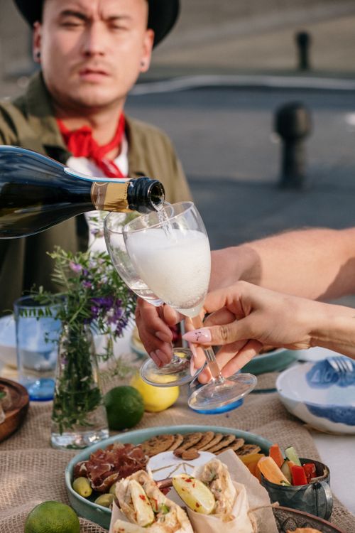 Free Friends enjoy a sunny outdoor gathering with wine and snacks, embracing togetherness and relaxation. Stock Photo