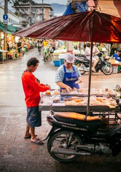 Vibrant street vendor scene in Thailand with locals selling food under an umbrella.