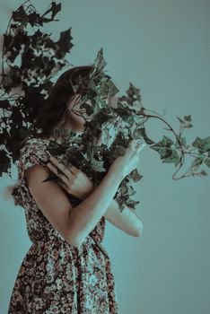 Artistic portrait of a woman in a floral dress holding ivy leaves, creating a mysterious and natural mood.