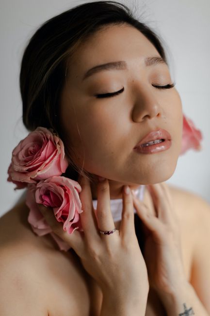 Serene portrait of a woman with pink roses, eyes closed, in a studio setting.
