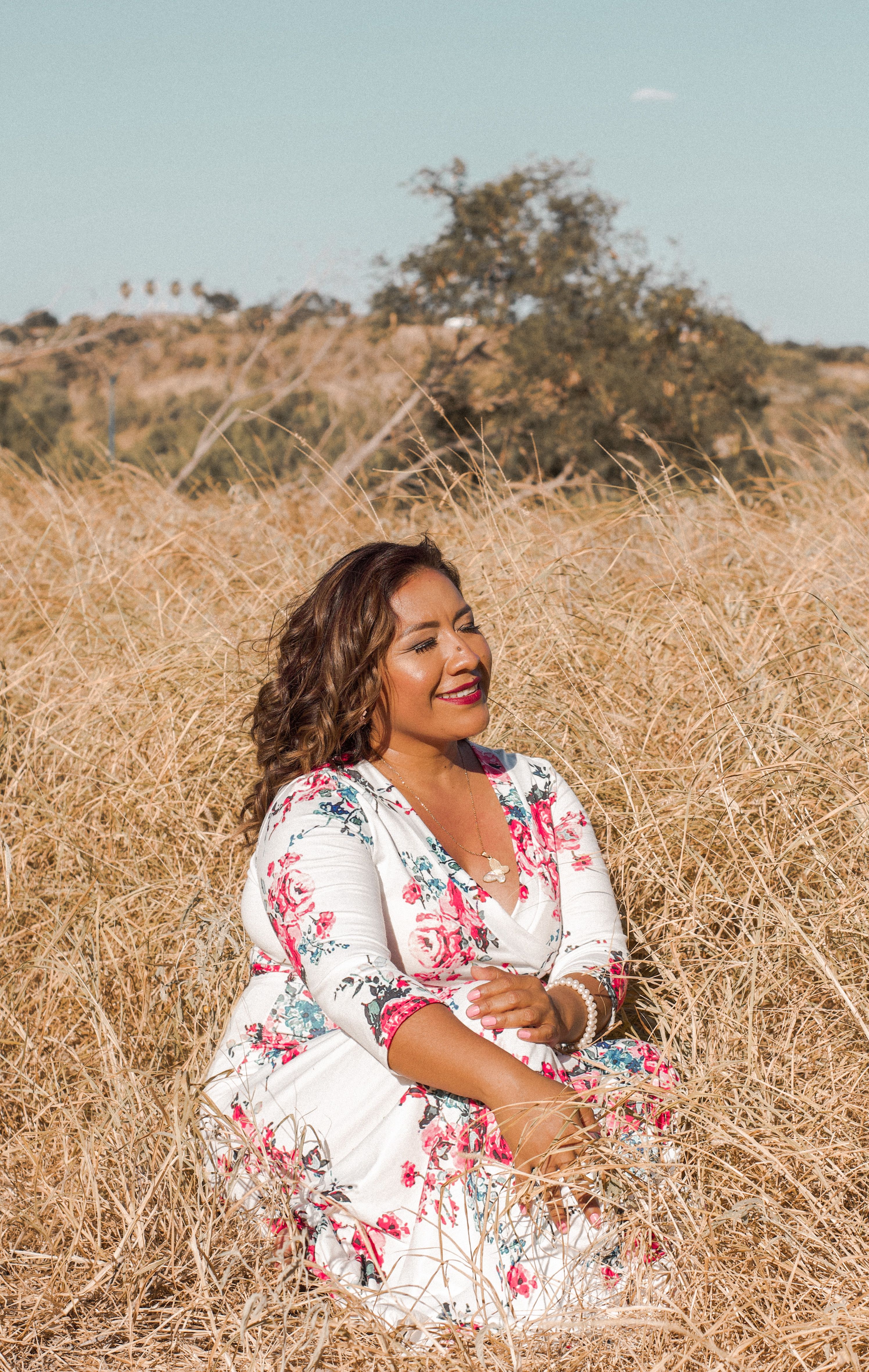 Woman In Floral Dress Sitting On Brown Grass Field · Free Stock Photo