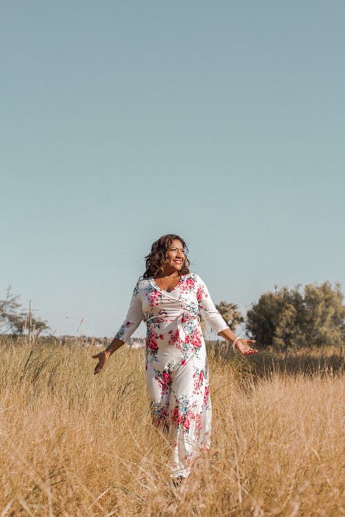 Woman in White and Red Floral Dress Standing on Brown Grass Field