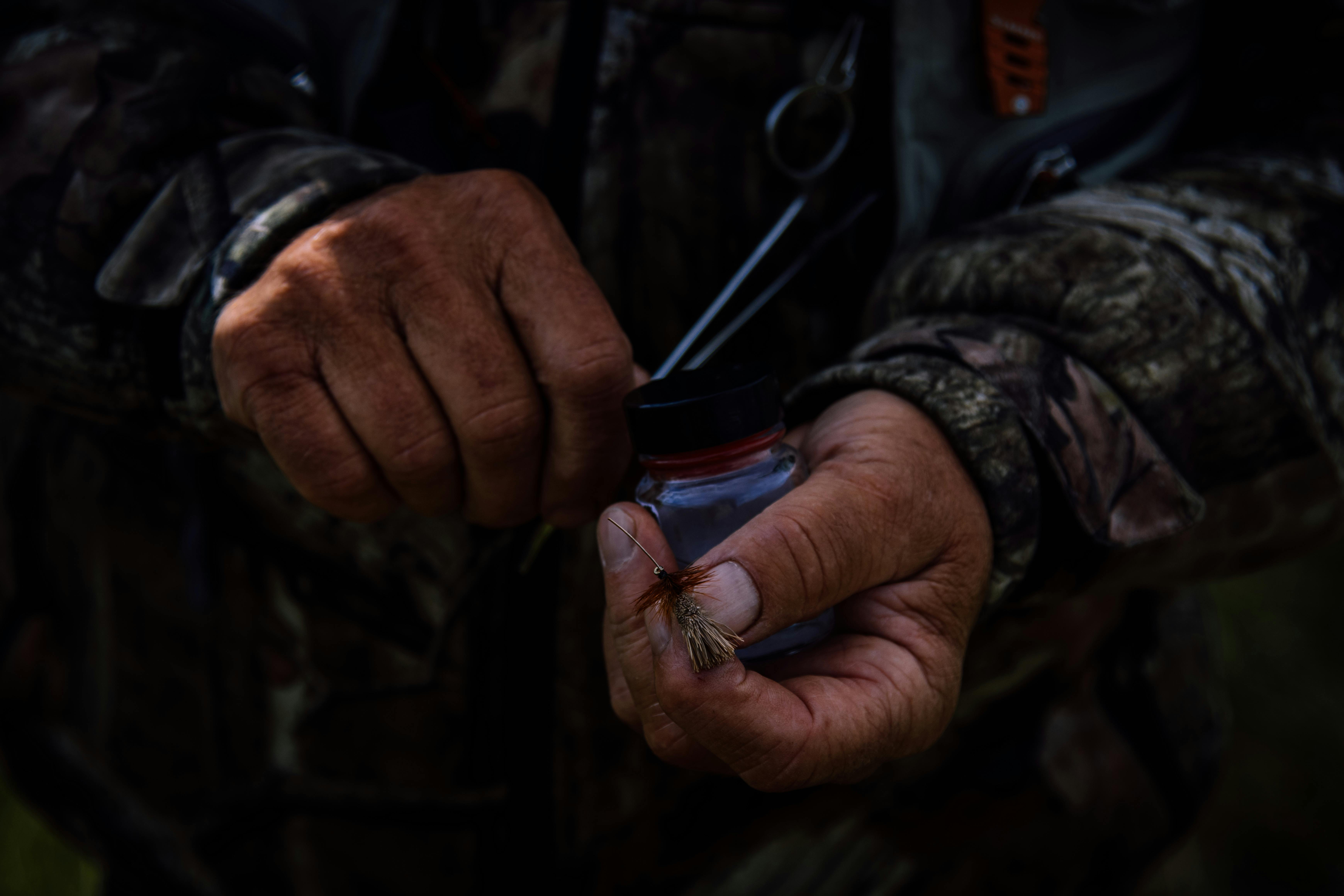 Close-up of a person preparing fly fishing equipment outdoors, showcasing detailed hands and gear.