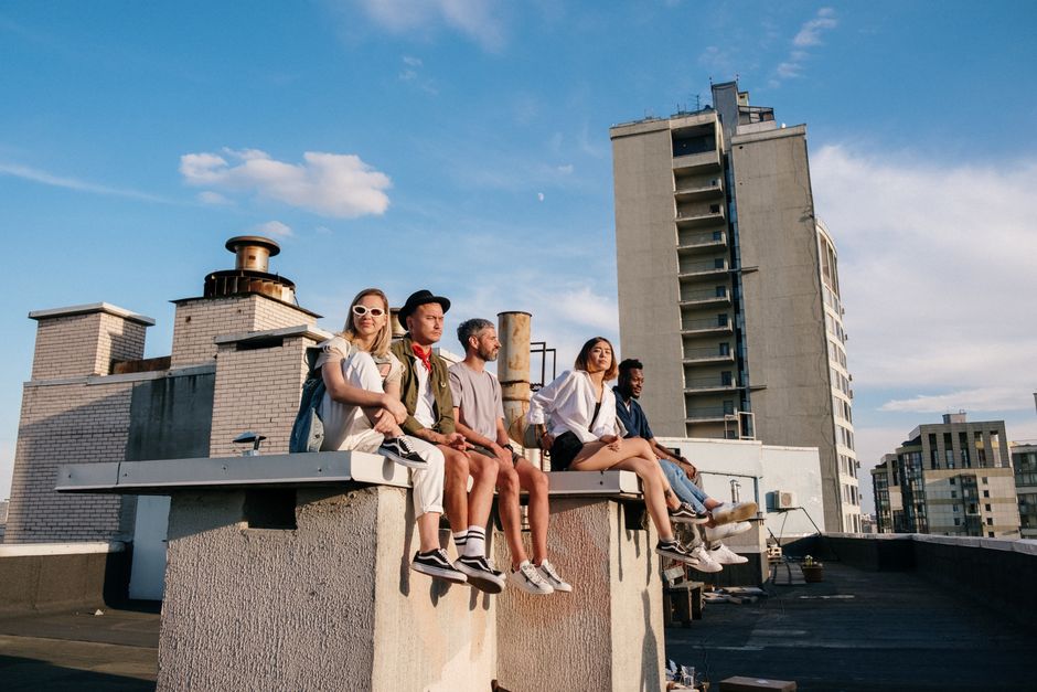 A diverse group of friends enjoying a summer evening on a rooftop, with city buildings in the background.