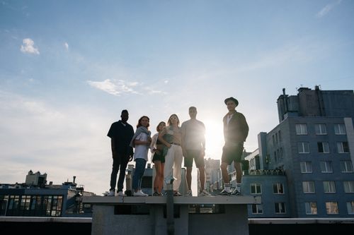 Free Group of young adults standing on a rooftop enjoying a sunny day, symbolizing freedom and friendship. Stock Photo