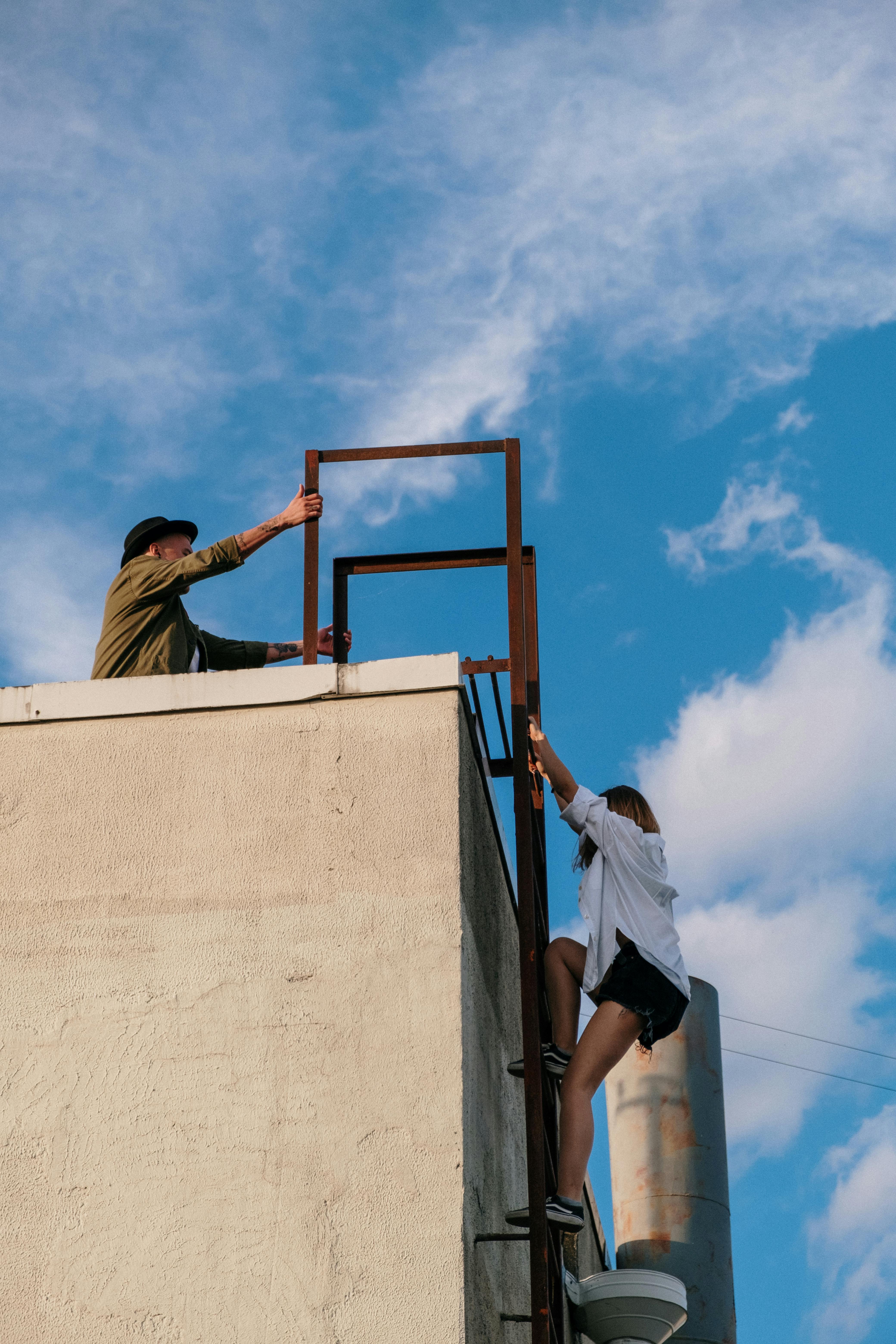 man in brown jacket and blue denim jeans climbing on brown concrete wall