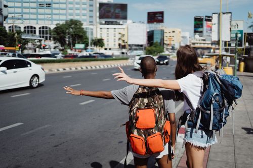 Free Two travelers with backpacks raising their arms at a busy city intersection. Stock Photo