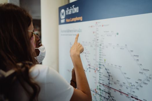 Two women in face masks pointing at a transport map, exploring new directions.