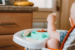 Baby in high chair eating food, surrounded by bananas in a kitchen setting.