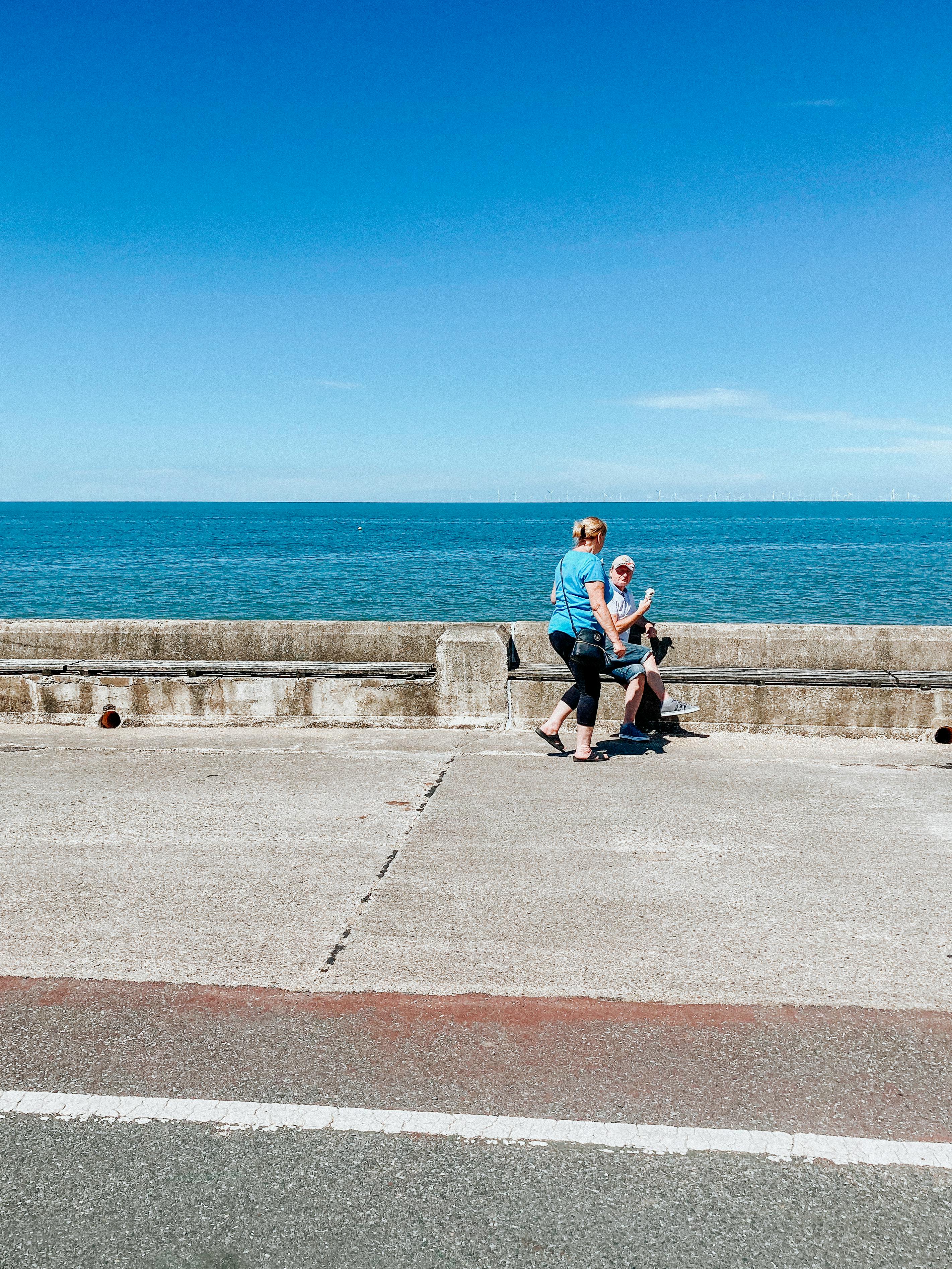 A man and a woman enjoying a peaceful seaside stroll under a clear blue sky.
