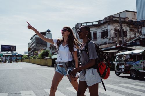 Free Two women, one pointing forward, explore a vibrant city street, showcasing joy and adventure. Stock Photo